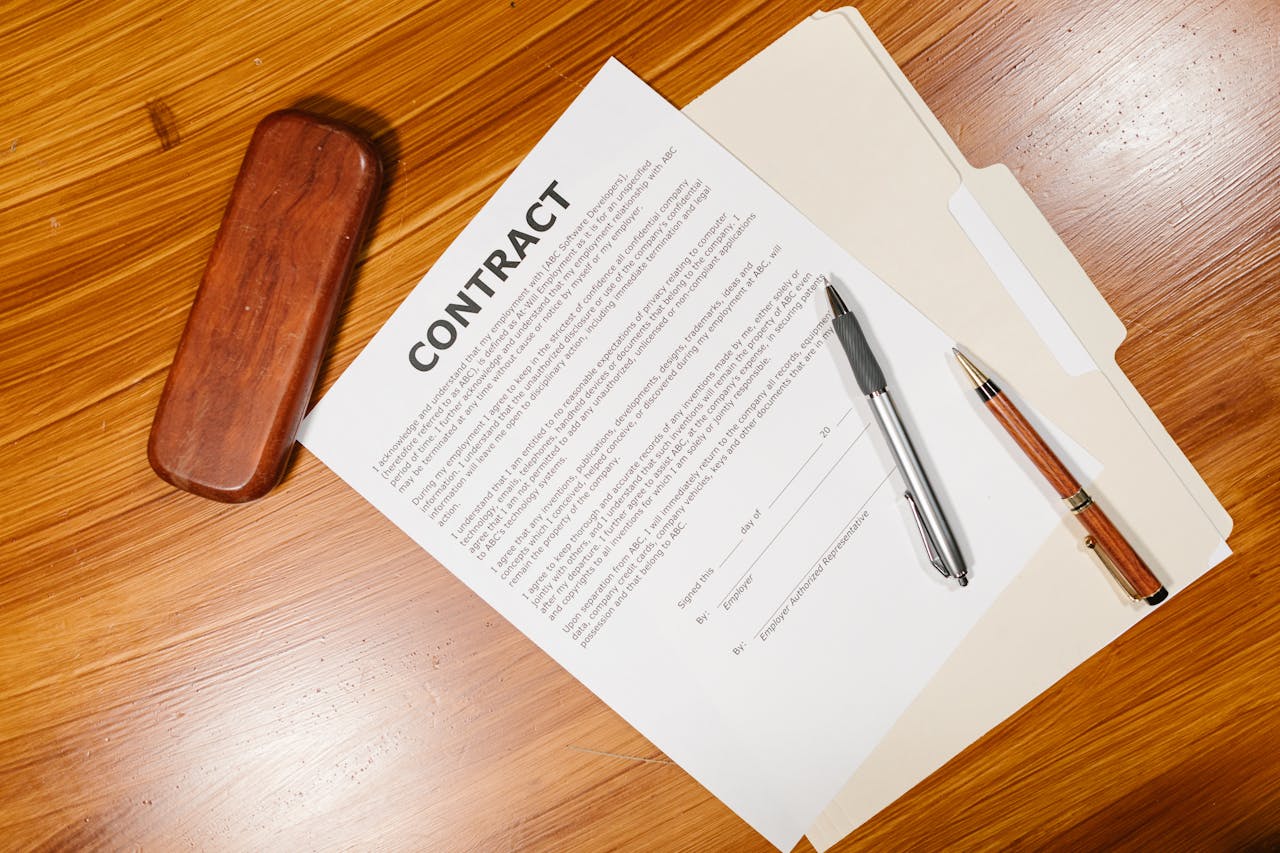 about-01 High-angle view of a contract document with pens and a case on a wooden table.